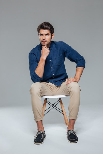 Pensive attractive casual young man sitting on chair - Foto, afbeelding