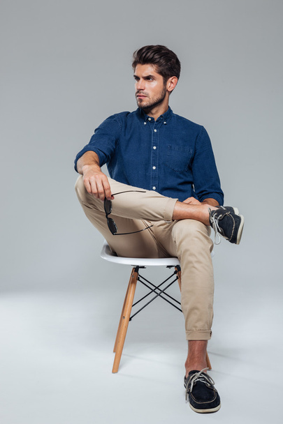 Handsome relaxed man holding suglasses and sitting on the chair - Фото, изображение