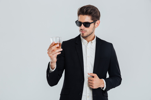 Businessman in suite and sunglasses looking at whiskey in glass - Fotó, kép
