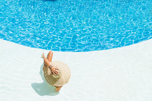beautiful woman in a hat sitting on the edge of the pool - Photo, Image