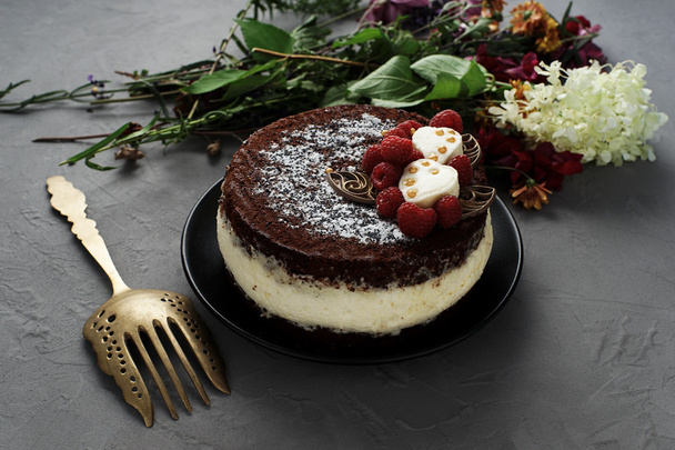 Cake, sprinkled with chocolate with a bouquet of flowers on a gray background.Cake covered with chocolate decorated with raspberries, with a bouquet of flowers on a gray background. - Valokuva, kuva