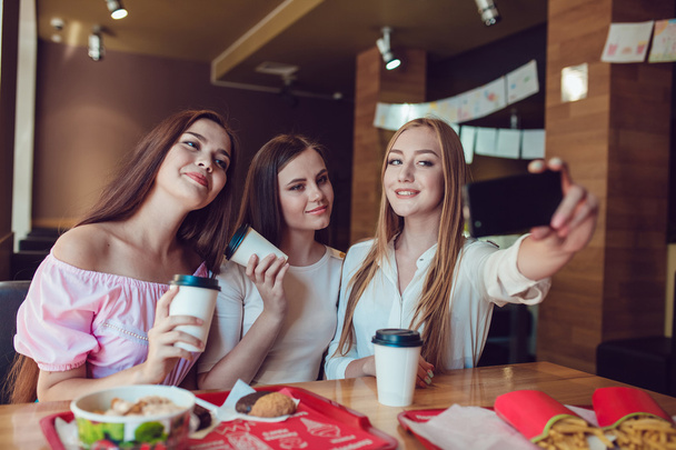 Three young girls are doing selfie in fast food restaurant - Φωτογραφία, εικόνα