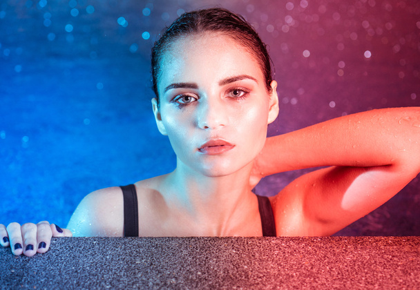 Closeup portrait of young woman beauty in pool during rainy evening with wet makeup looking into the camera - Photo, Image