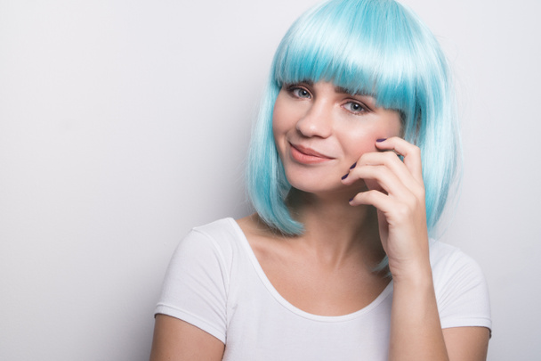 Mladá dívka v moderním futuristickém stylu s modrou parukou usmívající se a dívá se do kamery přes bílou stěnu pozadí s copyspace - Fotografie, Obrázek