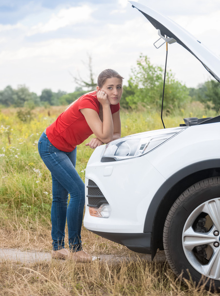 Розчарована жінка дивиться на зламаний автомобільний двигун на сільській дорозі
 - Фото, зображення
