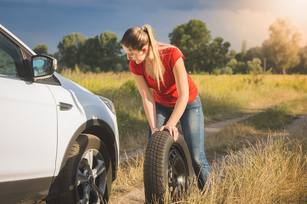 Beautiful woman rolling spare tire to change the flat one - Photo, Image