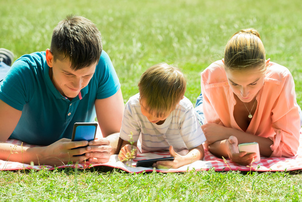 Family Laying Down In The Park With Their Smart Phones - Foto, Imagem