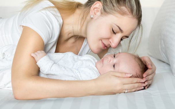 Portrait of beautiful young mother cuddling her baby boy on bed - Photo, Image