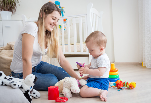 Mãe alegre e seu bebê no chão brincando com brinquedos
 - Foto, Imagem