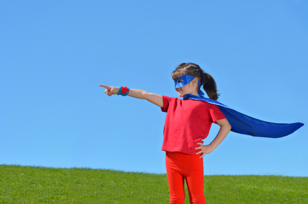 Menina super-herói aponta para o céu azul dramático
 - Foto, Imagem