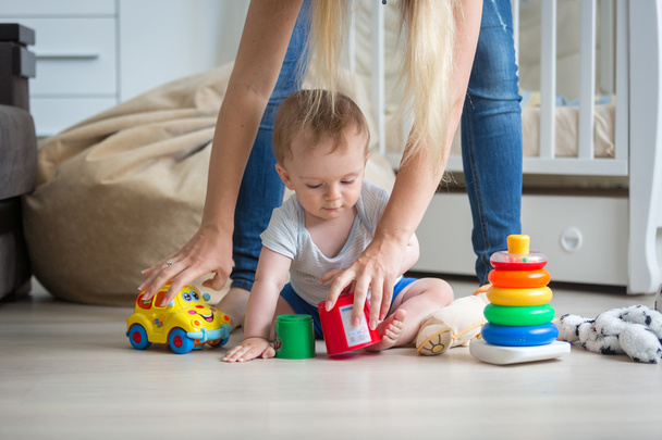 Mother giving toys to her 10 months old baby boy playing on floo - 写真・画像
