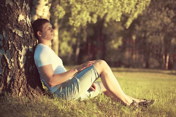 Relaxing man sitting under a tree with eyes closed meditating an - Φωτογραφία, εικόνα