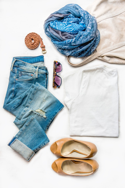 Collage weiblicher Kleidungsstücke. zerrissene Jeans, weißes Oberteil, braune High Heels und Accessoires über weißem Holzhintergrund. - Foto, Bild
