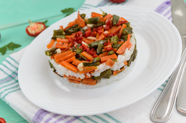 Ρύζι και τηγανητά λαχανικά (σπαράγγια φασόλια, καρότα) - vegan διατροφή γαρνιτούρα. Διακοσμημένα στρώματα της σαλάτας σε ένα άσπρο πιάτο. - Φωτογραφία, εικόνα