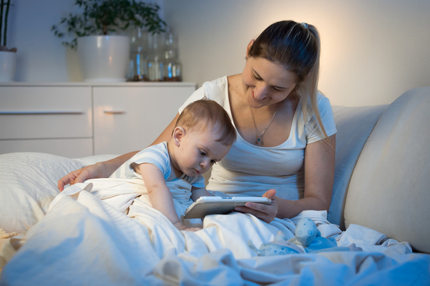 Bébé garçon assis sur le lit avec la mère et en utilisant une tablette numérique à
  - Photo, image