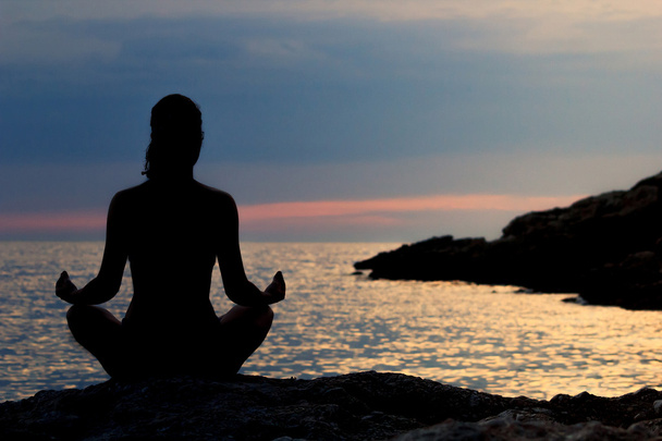 Siluetti nainen meditoi Lotus kannan meren rannalla auringonlaskun aikaan. Takanäkymä. Meditaatiokäsite
. - Valokuva, kuva