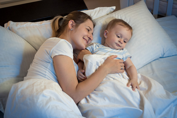 Smiling mother hugging her adorable baby in bed at night - Zdjęcie, obraz