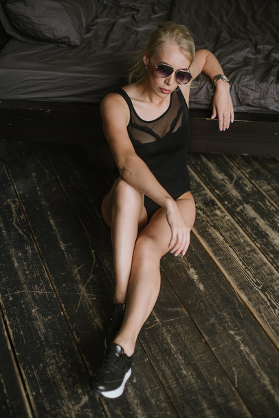 γυναίκα που ποζάρει με γυαλιά ηλίου που κάθεται δίπλα στο κρεβάτι με τα χέρια του σταυρωμένα στην αγκαλιά της - Φωτογραφία, εικόνα