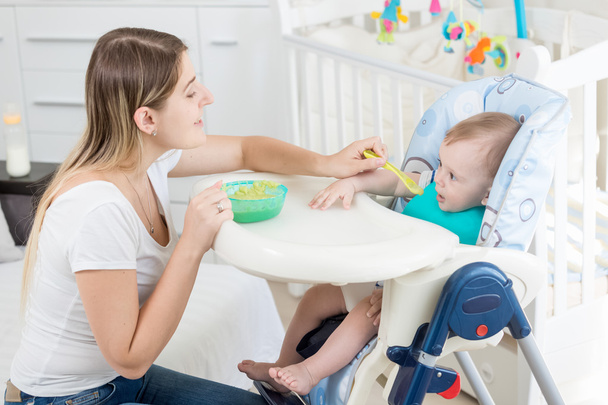 Portret van mooie vrouw voederen van 9 maanden oud jongetje sittin - Foto, afbeelding