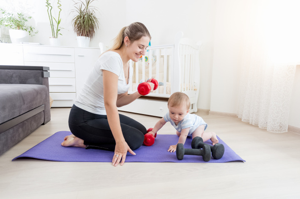 Sorrindo mãe com seu bebê menino se exercitando no chão com dumbbe
 - Foto, Imagem