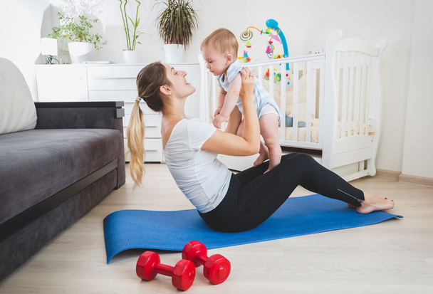 sSim madre jugando con su bebé en la colchoneta de fitness en casa
 - Foto, Imagen