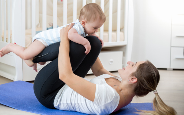 Mulher sorridente fazendo exercício de ioga com seu bebê na sala de estar
 - Foto, Imagem