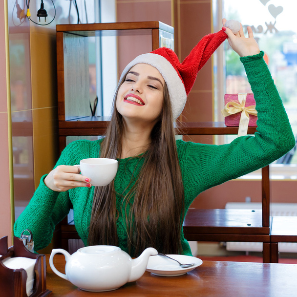 Joven mujer sonriente en rojo Santas sombrero beber té en la cafetería
 - Foto, Imagen