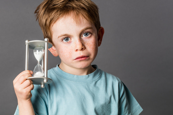sad young boy with big blue eyes holding egg timer - Фото, изображение