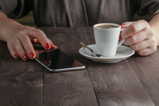 Жінка п'є каву в кафе і дивиться на екран телефону
 - Фото, зображення