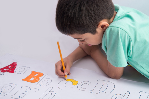 Μικρό παιδί αγόρι ζωγραφική και χρωματισμός αλφάβητο για τις εσωτερικές δραστηριότητές σας χαρτί - Φωτογραφία, εικόνα