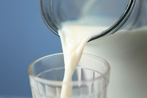 Milk pouring from a jug into a glass on blue background, closeup - Zdjęcie, obraz