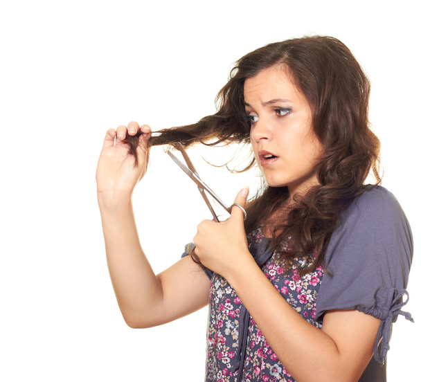 Красивая девушка с ножницами стрижет свои темные волнистые длинные волосы
 - Фото, изображение