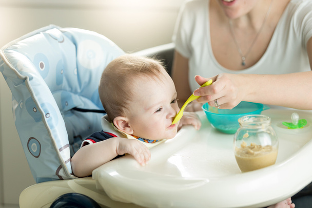 Mother feeding her 9 months old baby son sitting in child chair  - Photo, Image