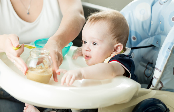 Мати годує хлопчика фруктовим пюре на кухні
 - Фото, зображення
