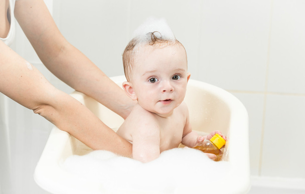 Мати купає свого хлопчика в пластиковій ванні
 - Фото, зображення