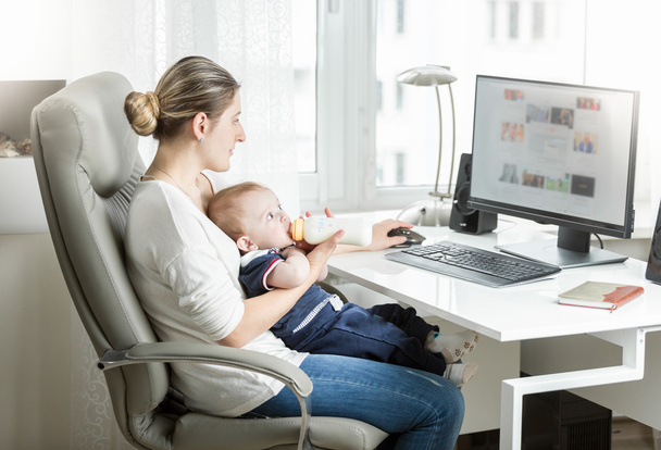 Mooie moeder werkt thuis kantoor en voeden van haar baby fro - Foto, afbeelding