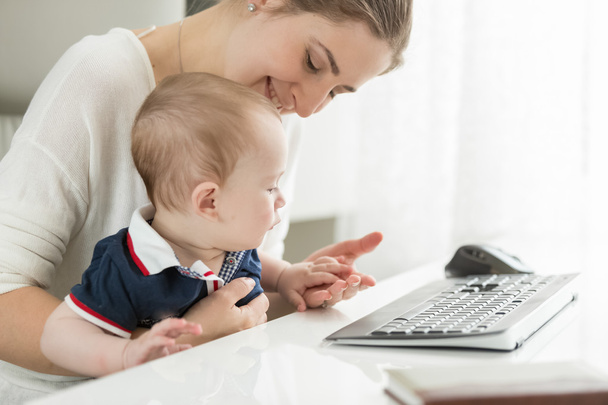 Mãe feliz sentado no computador e segurando seu bebê no colo
 - Foto, Imagem