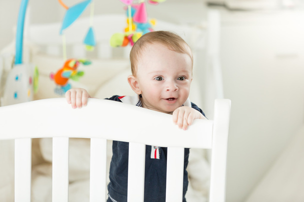 Adorable baby boy standing in bed and leaning on fence - Photo, Image