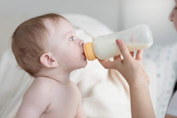 Portrait of baby boy sitting on bed and eating milk from bottle - Photo, Image