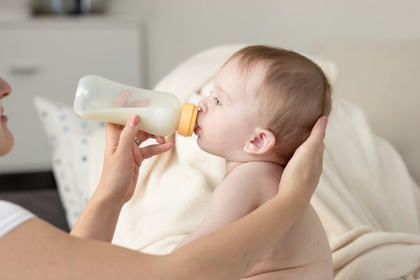 Primer plano de la madre dando leche del biberón a su bebé sittin
 - Foto, imagen