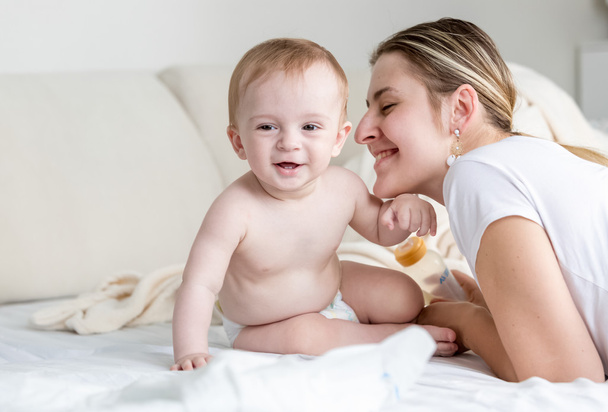 Gelukkig lachende baby aanbrengen met zijn moeder op bed in de slaapkamer - Foto, afbeelding