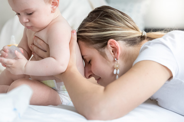 Portrait de jeune mère aimante embrassant son bébé jouant sur le lit
 - Photo, image