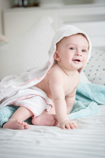 Smiling 9 months old baby boy sitting on bed covered in towel af - Φωτογραφία, εικόνα