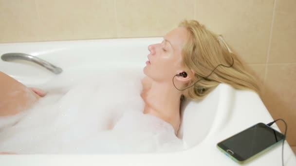 beautiful woman taking a bath and listening to music on headphones. cell phone - Materiał filmowy, wideo