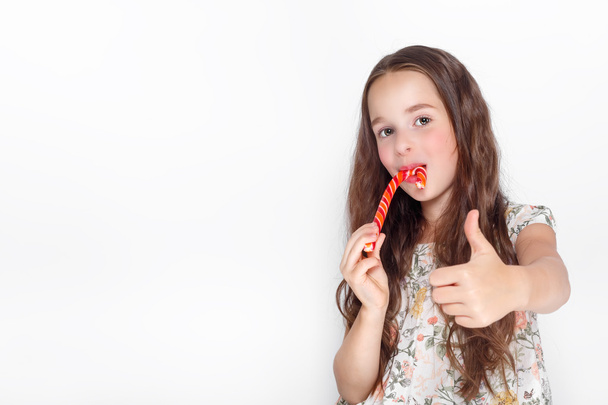 Joyeux, souriant petite fille mignonne mangeant des cristaux de canne à sucre. Dire d'accord. Poser contre un mur blanc
. - Photo, image