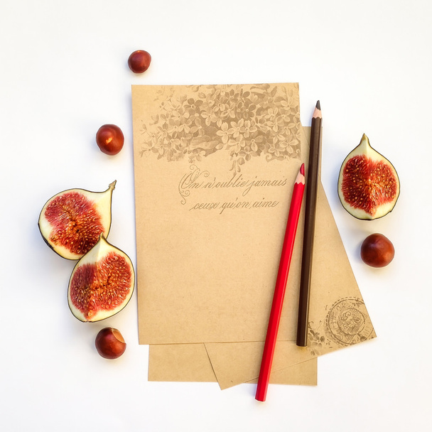 Empty paper sheets with pencils, fig fruits and chestnuts on background. Flat lay, top view - Foto, imagen