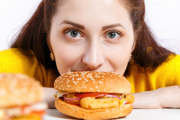 Девушка откусила огромный гамбургер. Нездоровое питание
.  - Фото, изображение