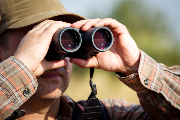 Man hunter with shotgun looking through binoculars in forest - 写真・画像