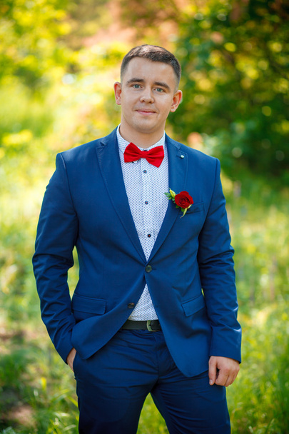 The groom in a blue suit with red butterfly and buttonhole-flower - Photo, Image