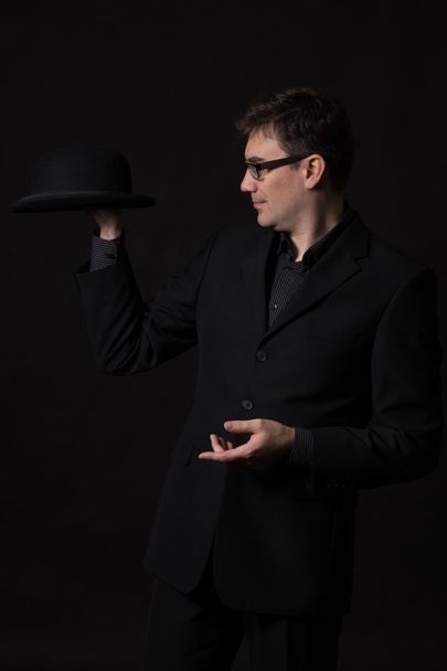Hombre con un traje negro sosteniendo un sombrero de jugador de bolos en una mano
 - Foto, Imagen